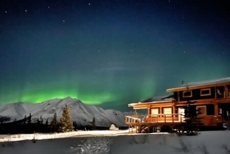 green aurora over mountains and a lodge in Alaska
